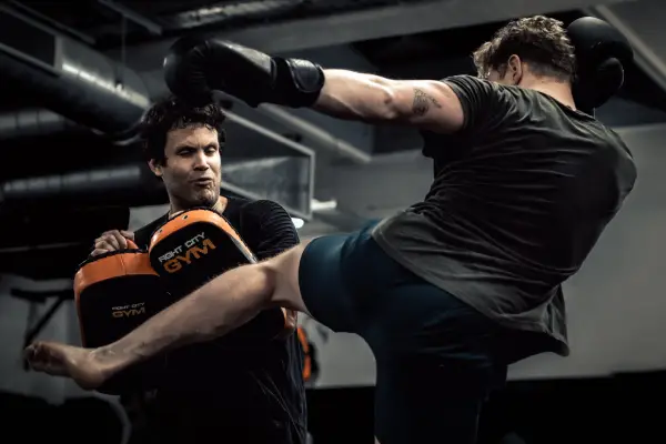 A man training in Muay Thai, practicing kicks on a pad